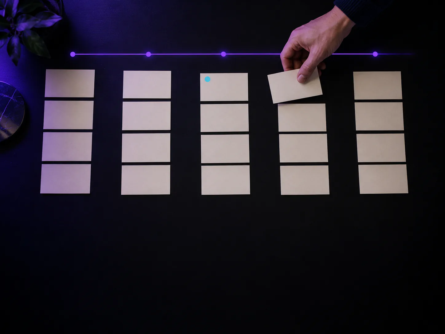 A hand moves a card along five columns of index cards laid out like a pipeline