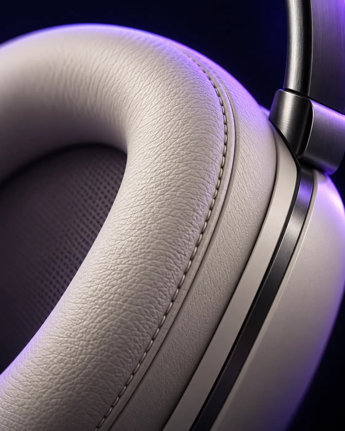 Close-up of a stone-white ear cushion showing the leather grain, stitched seam, and graphite hinge