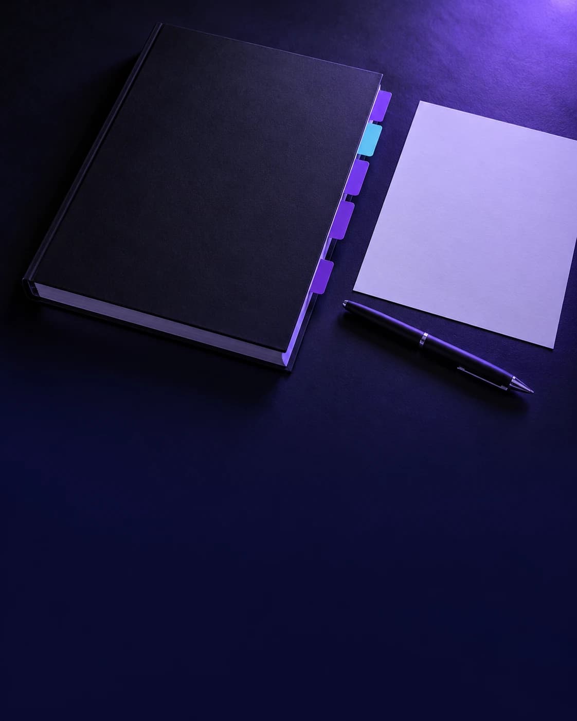 Closed black report with violet and cyan tab dividers beside a blank sheet of paper and a pen on a dark desk